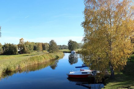 zeigt zwischen Wiesen einen Fluss mit Booten