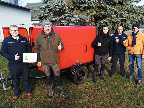 zeigt mehrere Personen, die um einen Schlauchtransportanhänger stehen